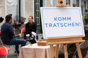 Aktion von Space and Place. Im Vordergrund steht ein Schild mit der Aufschrift "Komm Tratschen!"