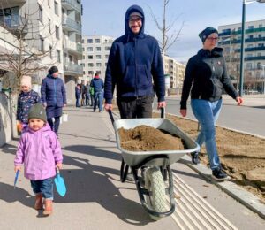 Eine Familie mit Kind zieht mit einer Scheibtruhe aus, um den öffentlichen Raum in der Seestadt zu begrünen