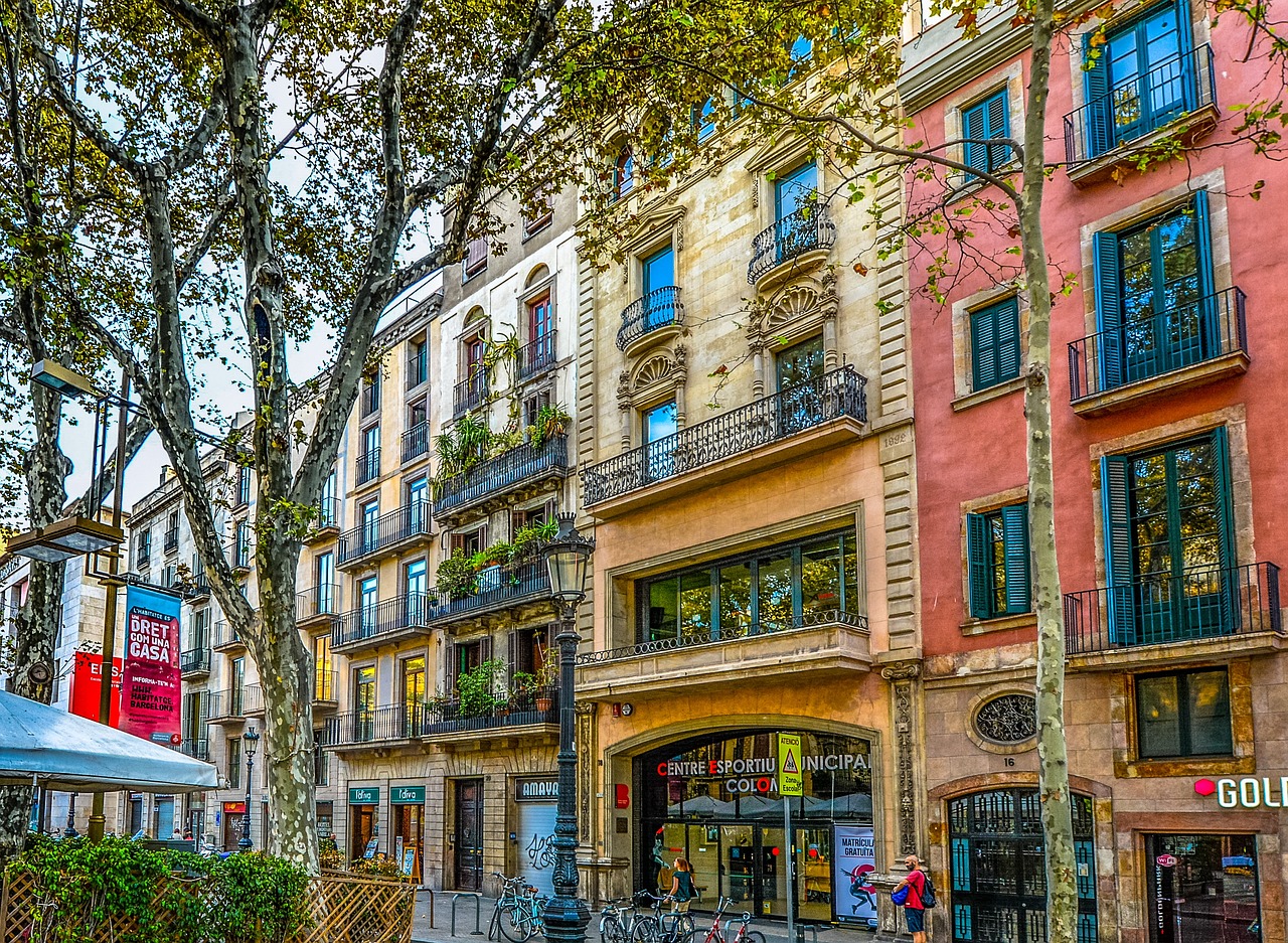 Häuserfronten in Barcelona, davor ist eine belebte Straße mit Baum zu sehen
